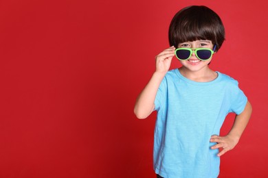 Photo of Cute little boy with sunglasses on red background, space for text