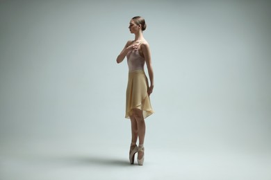 Young ballerina practicing dance moves on light grey background