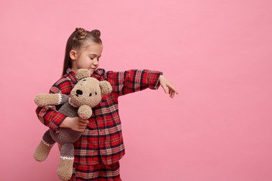Photo of Girl in pajamas with toy bear sleepwalking on pink background, space for text