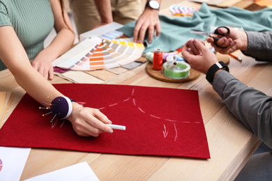 Photo of Fashion designers creating new clothes at table in studio, closeup