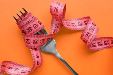 Photo of Fork with measuring tape on orange background, top view. Diet concept