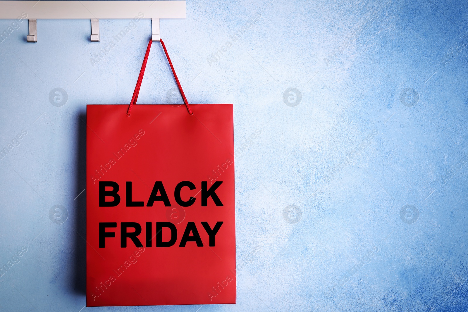 Image of Paper shopping bag with phrase BLACK FRIDAY on rack near blue wall, space for text
