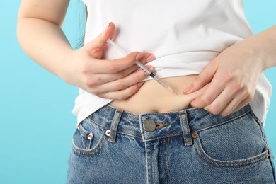 Photo of Diabetes. Woman making insulin injection into her belly on light blue background, closeup