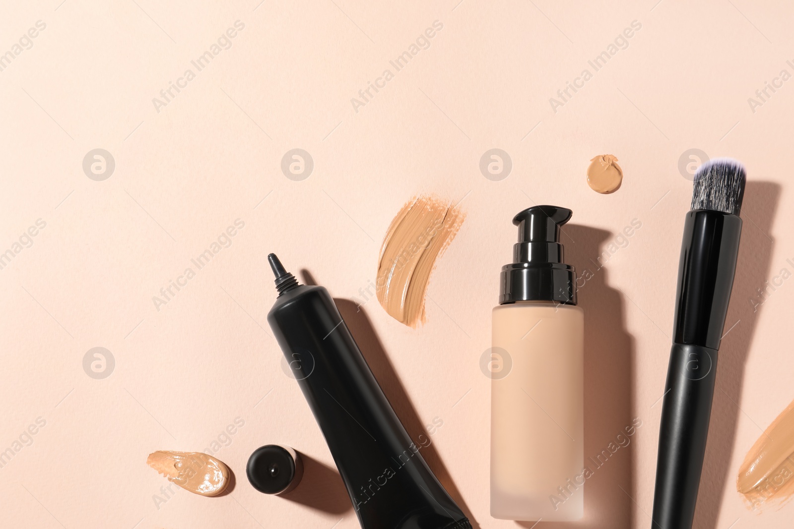 Photo of Liquid foundations, swatches and makeup brush on beige background, flat lay. Space for text