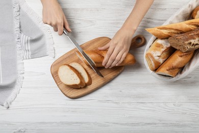 Photo of Woman cutting freshly baked baguette at white wooden table, top view