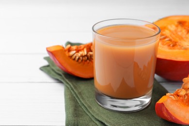 Photo of Tasty pumpkin juice in glass and cut pumpkin on white wooden table. Space for text