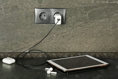 Photo of Tablet charging from electric socket on dark grey table indoors