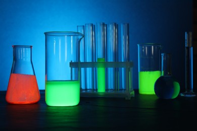Photo of Laboratory glassware with luminous liquids on table against light blue background