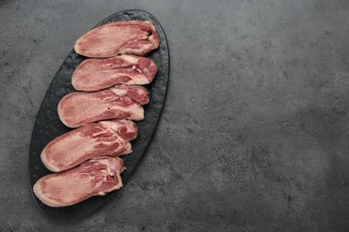 Photo of Raw beef tongue pieces on grey table, top view and space for text
