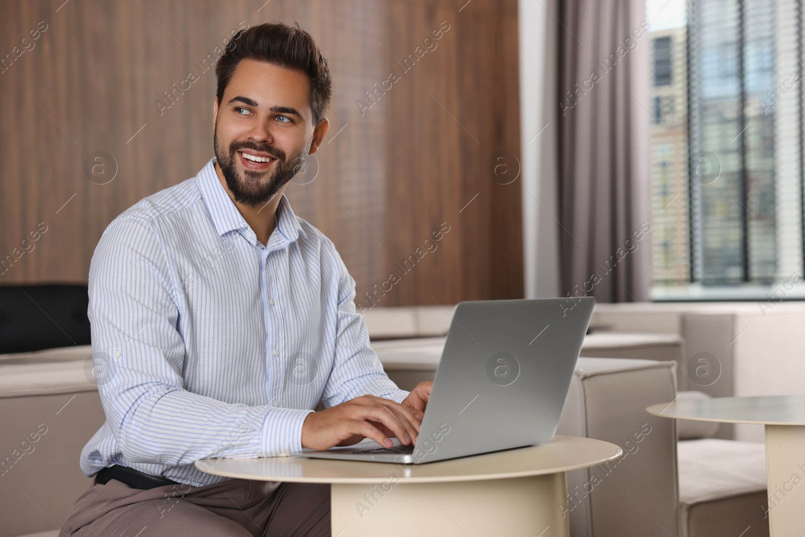 Photo of Happy young man working on laptop at table in office. Space for text