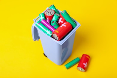 Many used batteries in recycling bin on yellow background