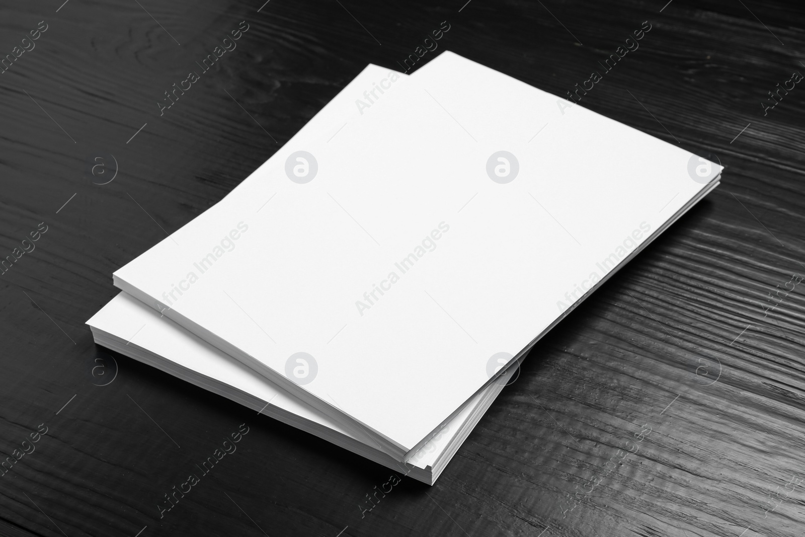 Photo of Stack of blank paper sheets for brochure on black wooden background. Mock up