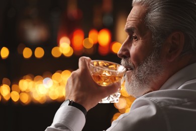 Photo of Senior man drinking whiskey against blurred lights, closeup