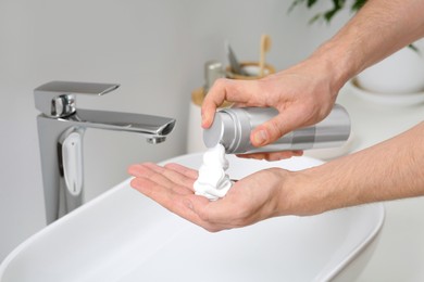 Photo of Man applying shaving foam onto hand in bathroom, closeup