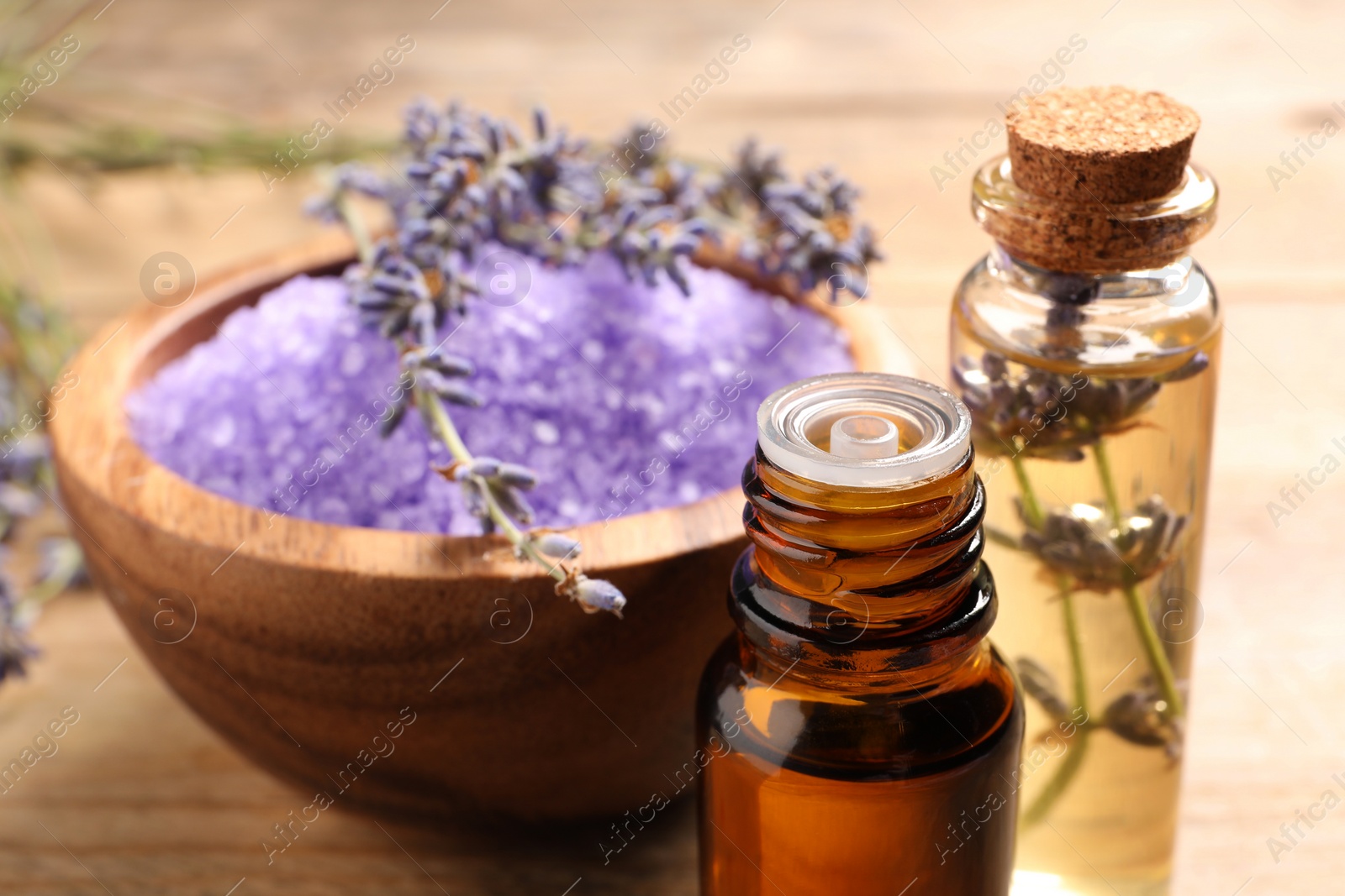 Photo of Bowl of sea salt, essential oil and lavender flowers on wooden table, closeup