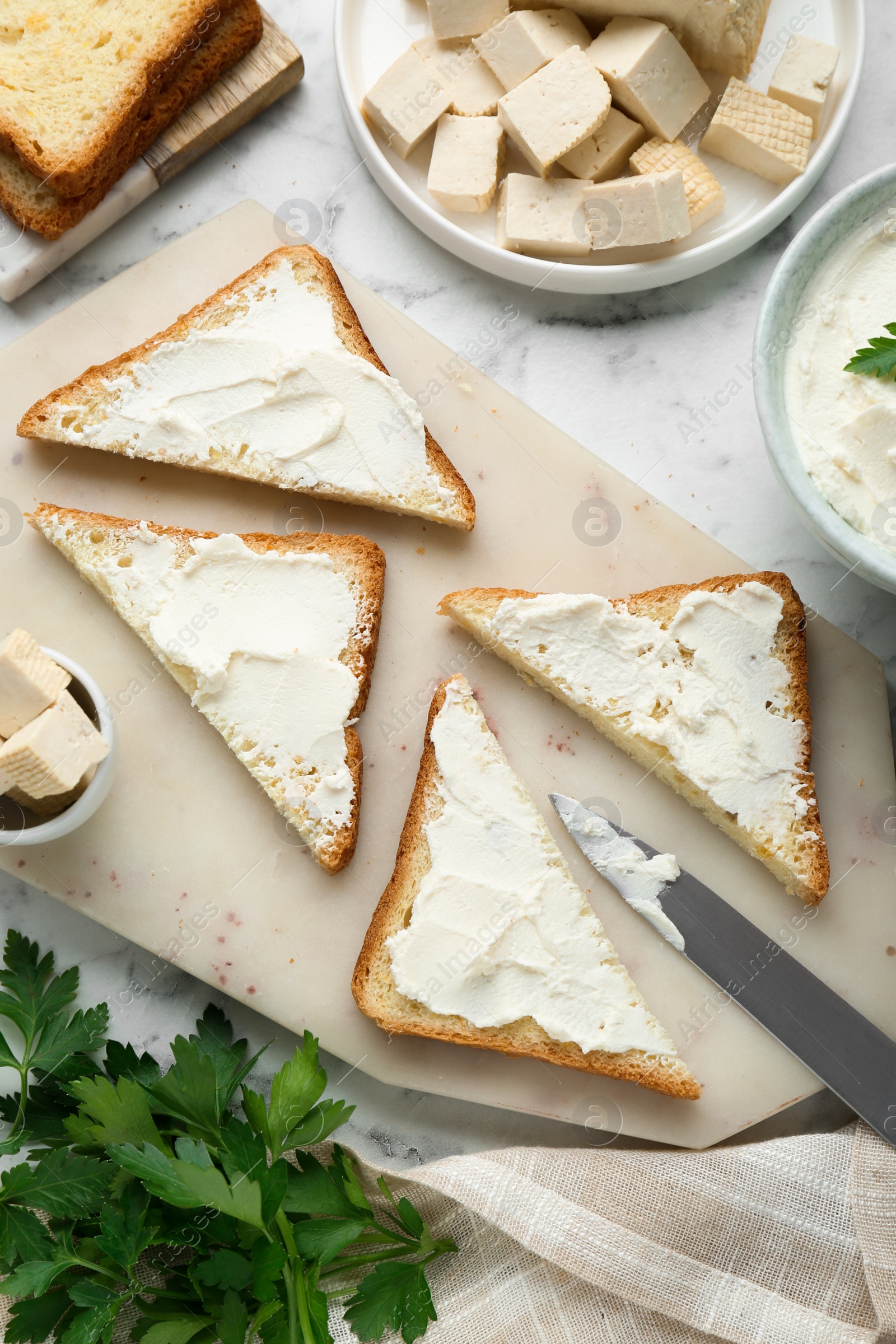 Photo of Delicious toasts with tofu cream cheese and parsley on white marble table, flat lay