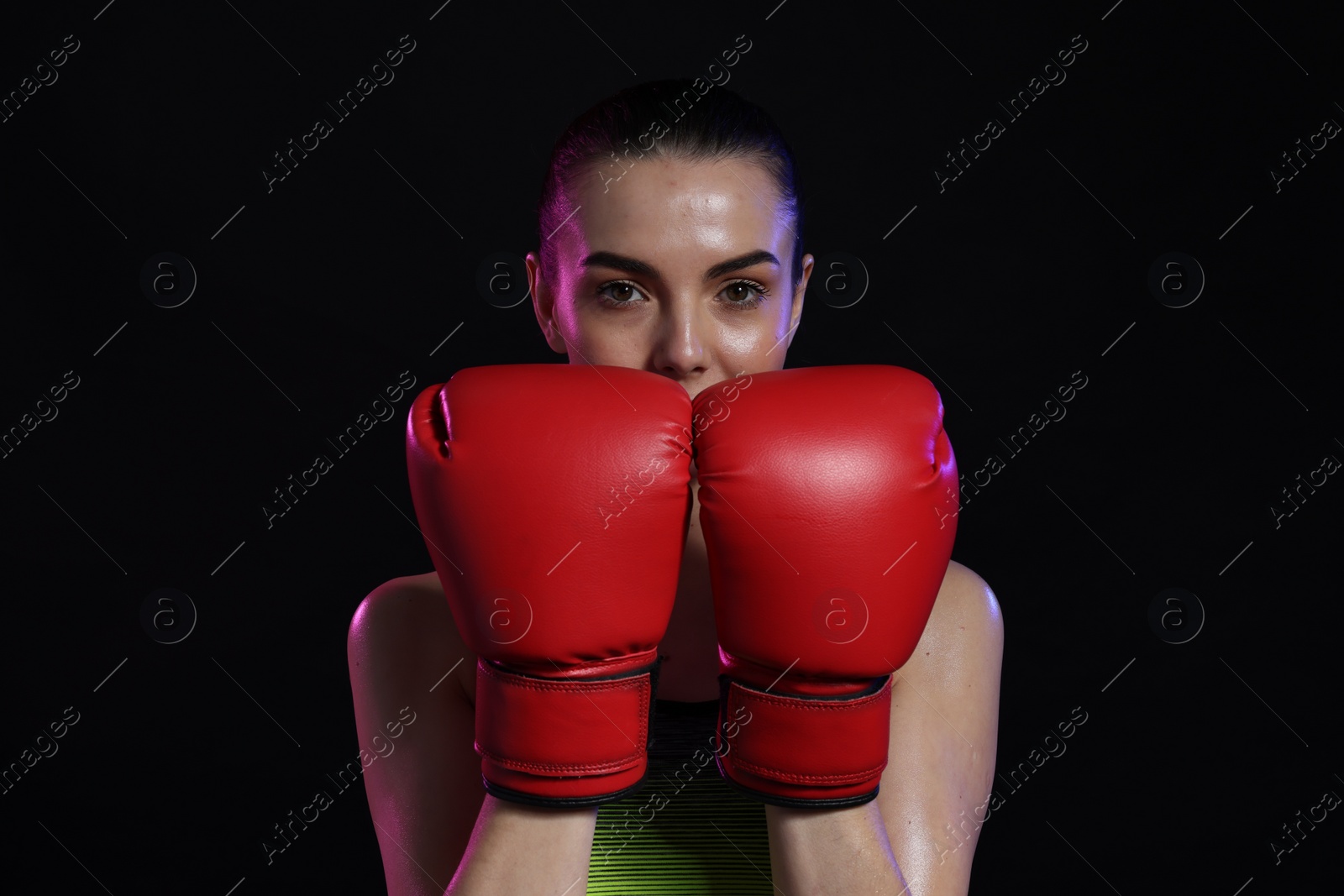 Photo of Portrait of beautiful woman wearing boxing gloves in color lights on black background