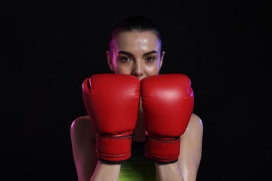 Photo of Portrait of beautiful woman wearing boxing gloves in color lights on black background