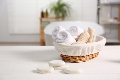 Photo of Basket with spa herbal bags, towels and stones on white wooden table in bathroom, space for text