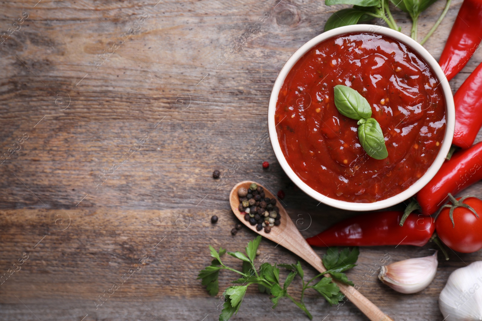 Photo of Flat lay composition with bowl of chili sauce and ingredients on wooden table. Space for text