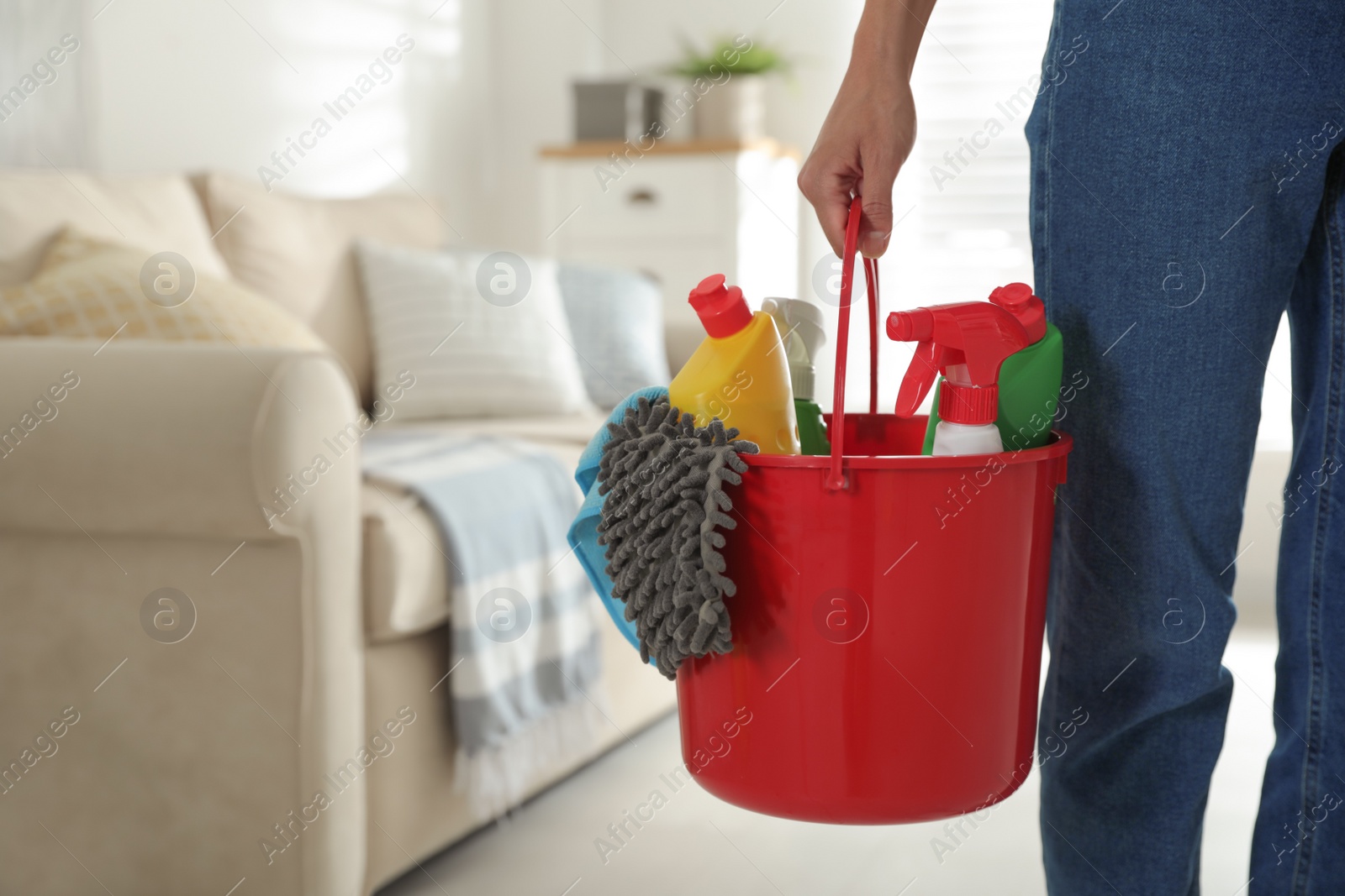 Photo of Woman holding bucket with different cleaning supplies at home, closeup. Space for text