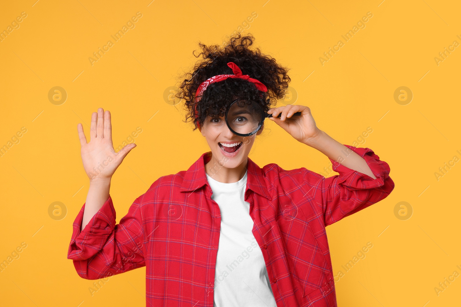 Photo of Happy young woman looking through magnifier glass on yellow background