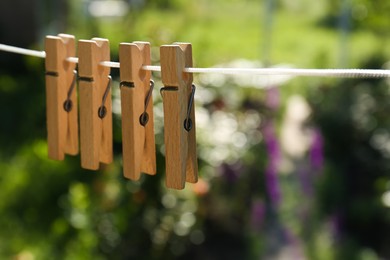 Wooden clothespins hanging on washing line outdoors, closeup. Space for text