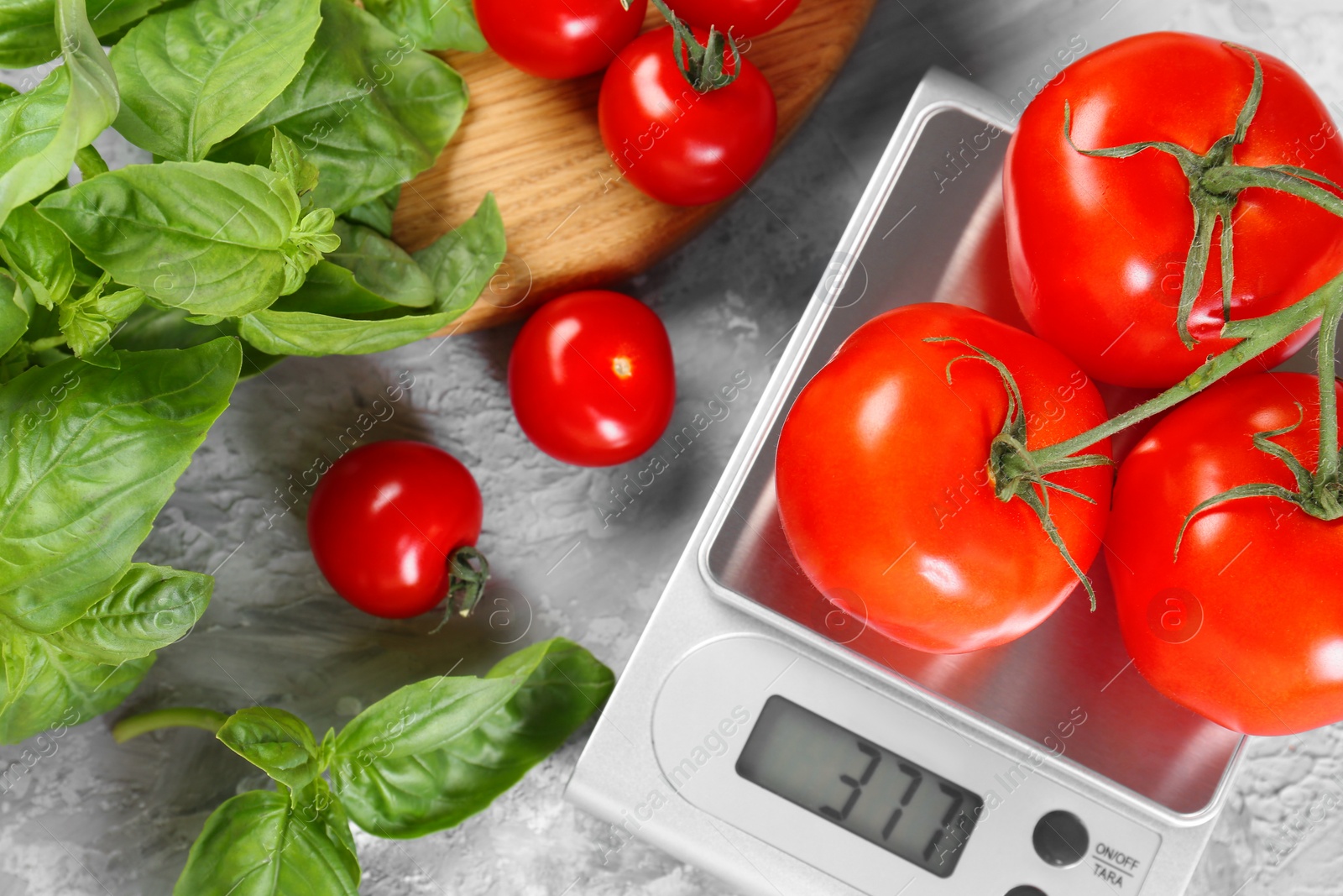 Photo of Kitchen scale with tomatoes and basil on grey textured table, flat lay