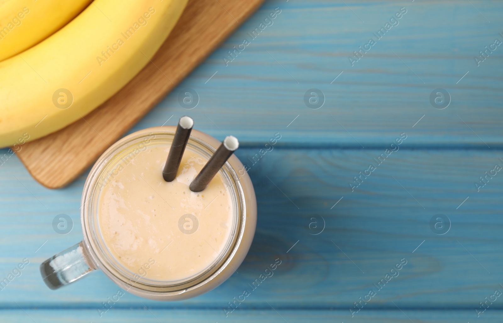 Photo of Mason jar with banana smoothie on light blue wooden table, flat lay. Space for text