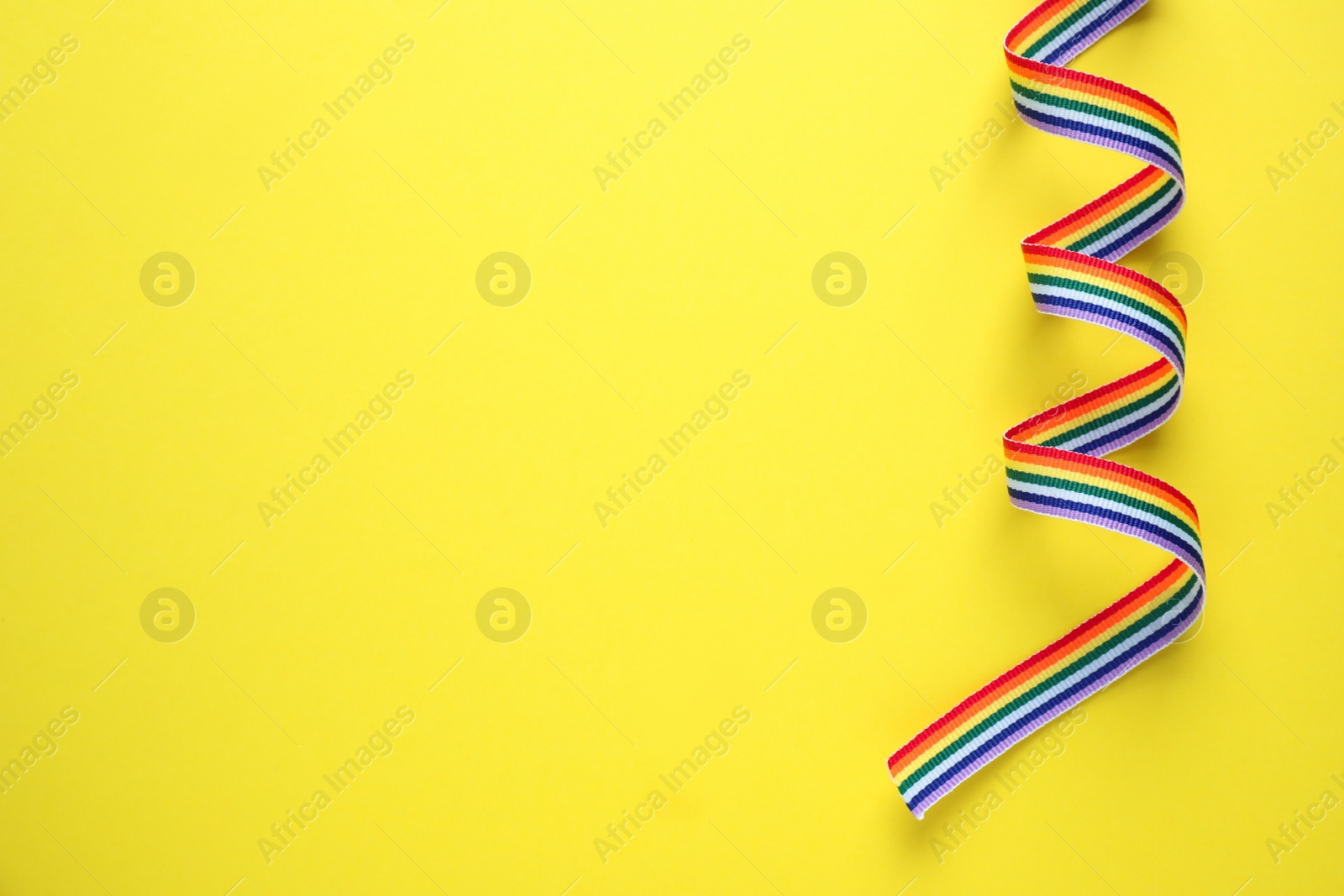 Photo of Top view of rainbow ribbon on yellow background, space for text. Gay symbol