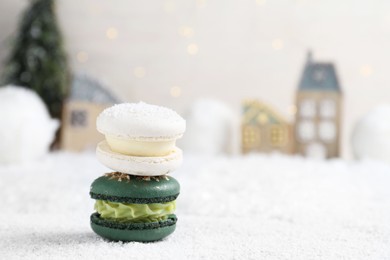 Different decorated Christmas macarons on table with artificial snow, space for text