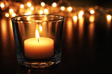 Photo of Wax candle burning on table in darkness, closeup