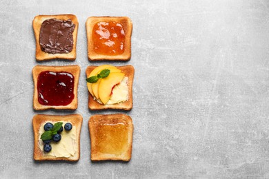 Tasty toasts with different spreads and fruits on light grey table, flat lay. Space for text