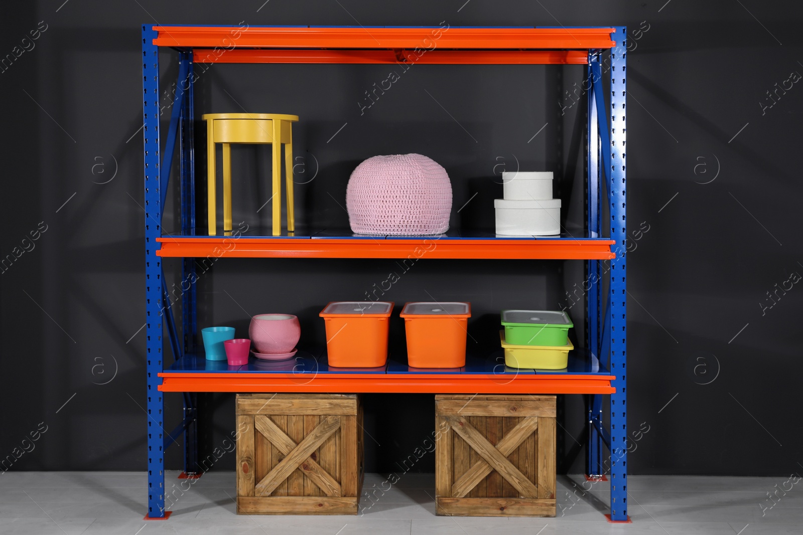 Photo of Metal shelving unit with wooden crates and different household stuff near black wall indoors