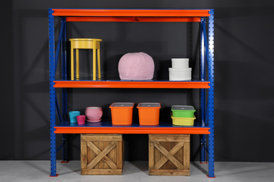 Photo of Metal shelving unit with wooden crates and different household stuff near black wall indoors