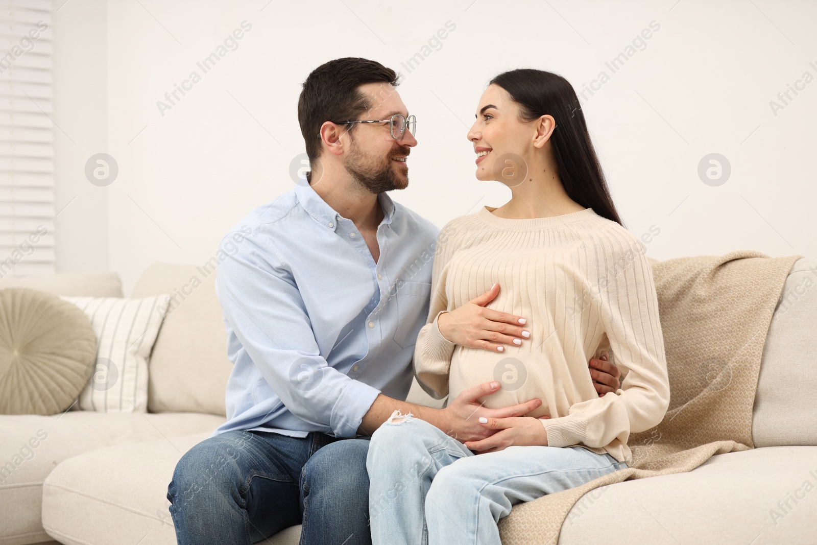 Photo of Happy pregnant woman with her husband on sofa at home