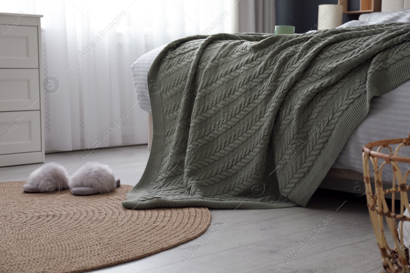 Photo of Comfortable bed with knitted green plaid in stylish room interior