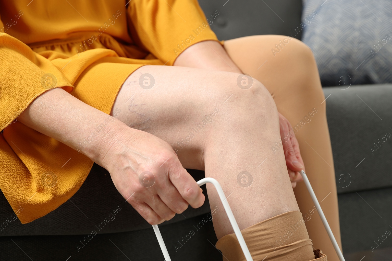 Photo of Woman putting on compression tights with stocking donner in living room, closeup. Prevention of varicose veins