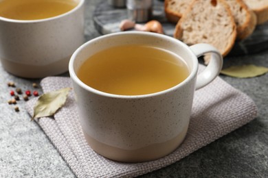Photo of Hot delicious bouillon in cups on grey table