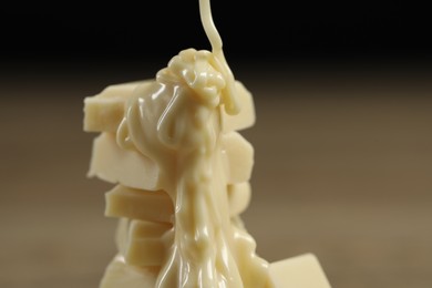 Photo of Pouring tasty white chocolate paste onto pieces against blurred background, closeup. Space for text