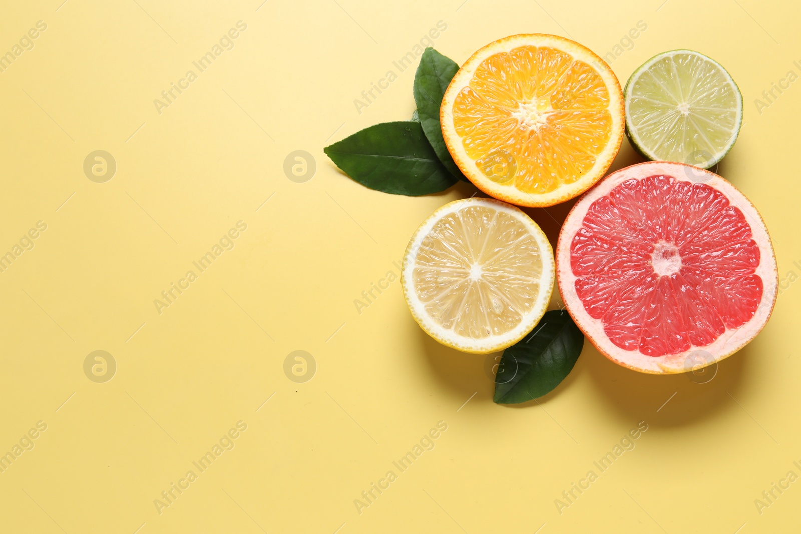 Photo of Different cut citrus fruits and leaves on yellow table, flat lay. Space for text