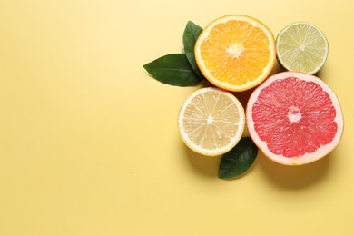 Different cut citrus fruits and leaves on yellow table, flat lay. Space for text