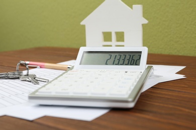 Photo of Calculator, house model, keys and documents on wooden table. Real estate agent's workplace