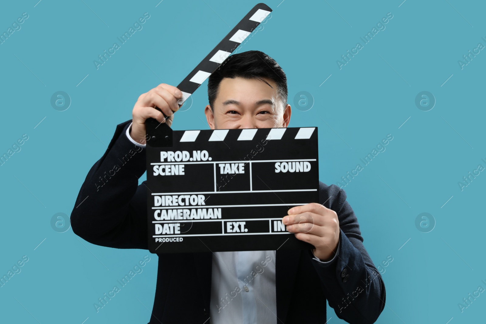 Photo of Happy asian actor with clapperboard on light blue background. Film industry