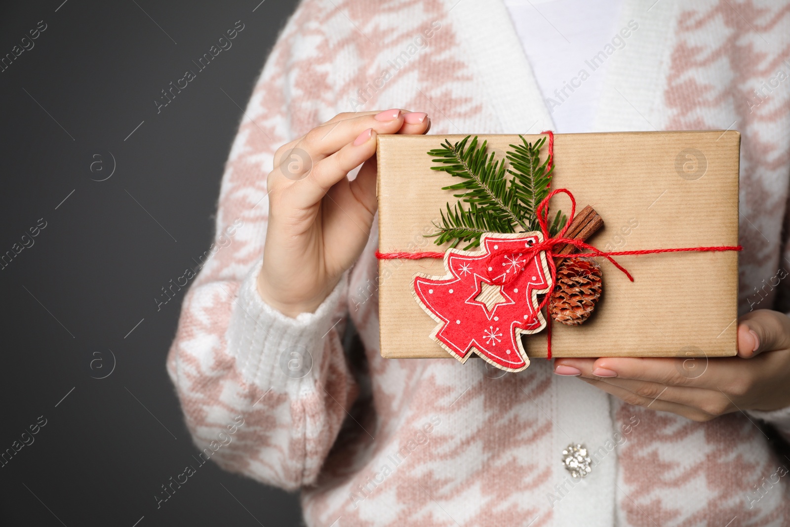 Photo of Woman holding beautifully wrapped Christmas gift box on dark grey background, closeup. Space for text