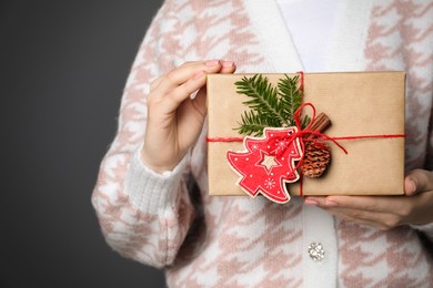 Woman holding beautifully wrapped Christmas gift box on dark grey background, closeup. Space for text