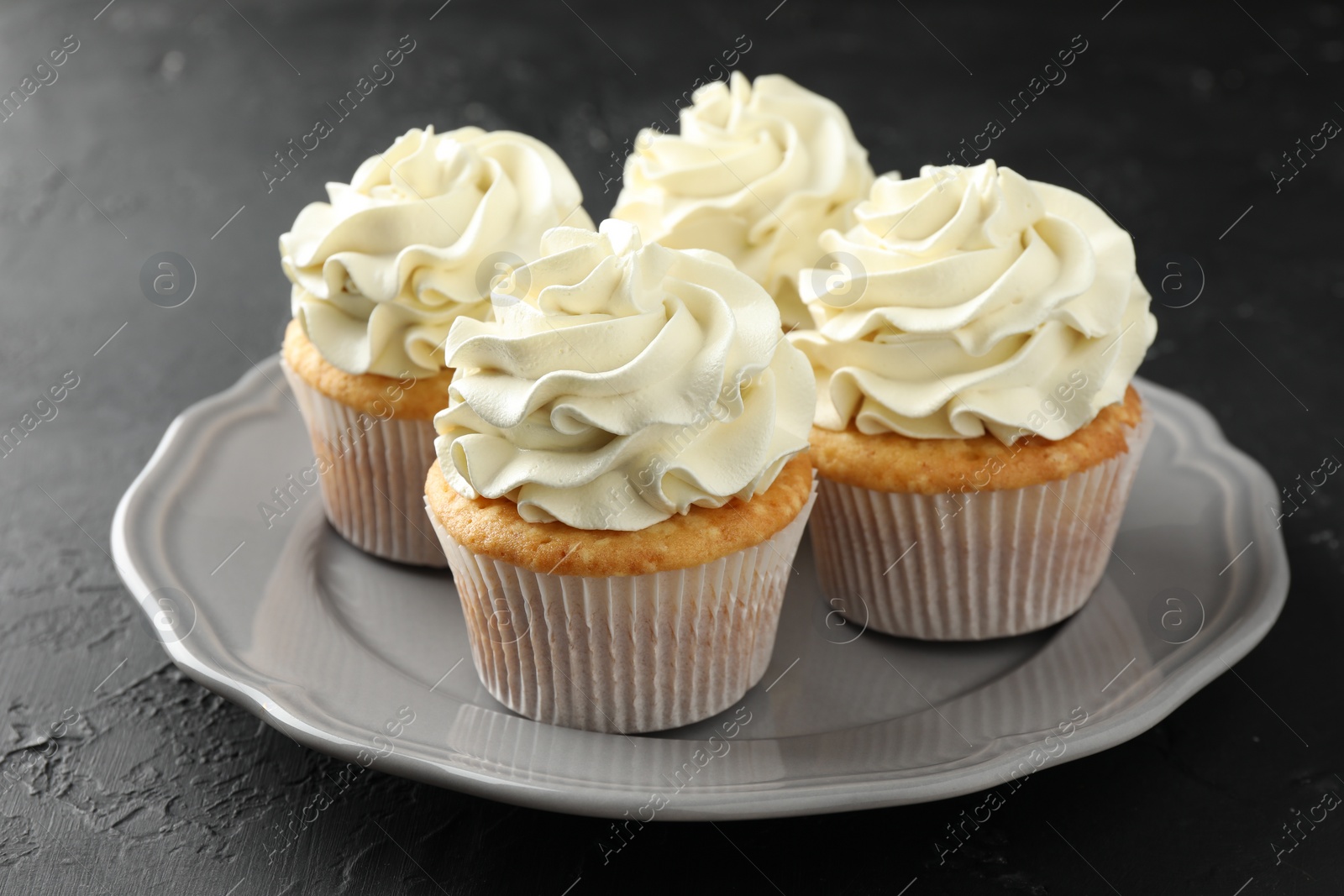 Photo of Tasty cupcakes with vanilla cream on black table, closeup