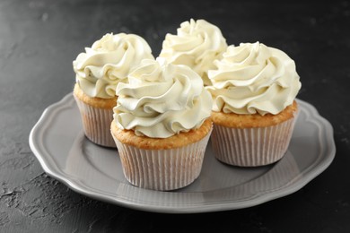 Photo of Tasty cupcakes with vanilla cream on black table, closeup