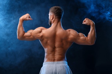 Photo of Young bodybuilder with muscular body in smoke on color background, back view