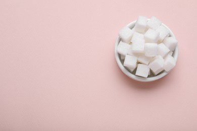 Photo of Refined white sugar cubes in bowl on pink background, top view. Space for text
